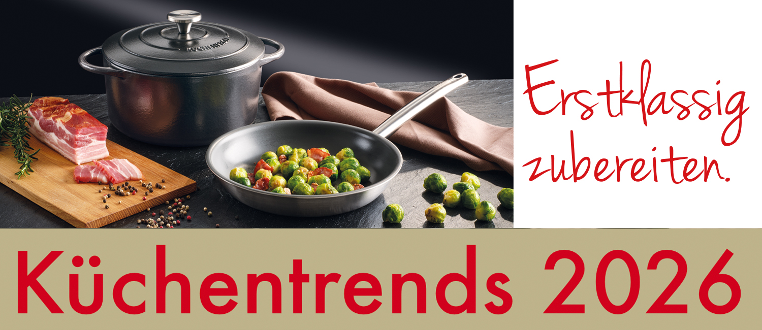 Edelstahl-Kochtopf und Bratpfanne mit Rosenkohl und Speck, daneben Schinken auf einem Holzbrett. Schriftzug: Küchentrends 2026, Erstklassig zubereiten.
